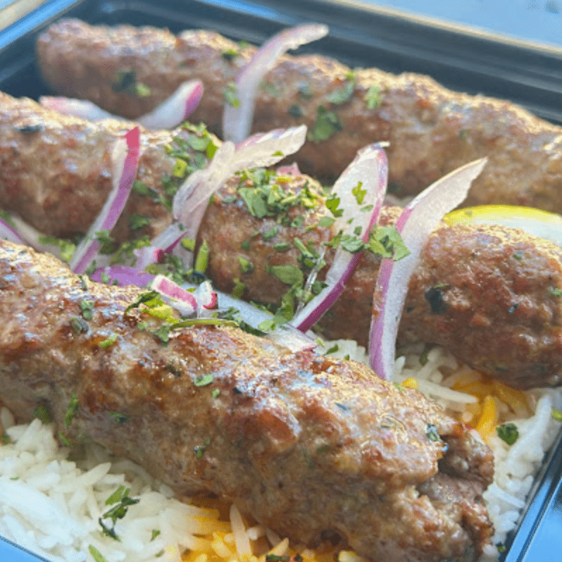 Minced meat kebabs on rice, garnished with red onion and herbs.